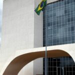 Edifício do Tribunal de Justiça em Brasília com bandeira a meio mastro, simbolizando luto pela morte de desembargador.