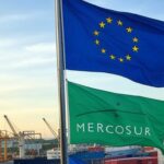Bandeiras da UE e Mercosul no Porto de Santos, representando acordo comercial histórico entre blocos econômicos.