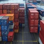 Porto marítimo no Brasil com contêineres e navios, simbolizando tarifas comerciais impostas a negociações com o Irã.