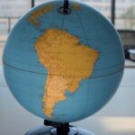 Imagem de globo terrestre destacando Portugal com símbolos de polarização e instabilidade global, em ambiente brasileiro.