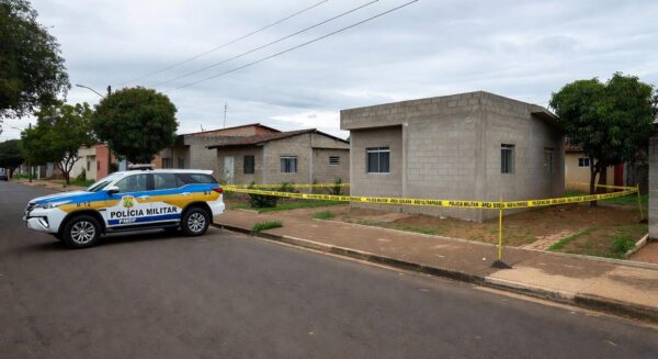 Viatura da Polícia Militar em rua residencial no Gama, Brasília, com fita de isolamento em cena de crime.