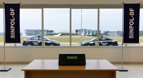 Urna eletrônica em eleição para diretoria do Sinpol-DF, com viaturas da Polícia Civil do DF ao fundo em Brasília.